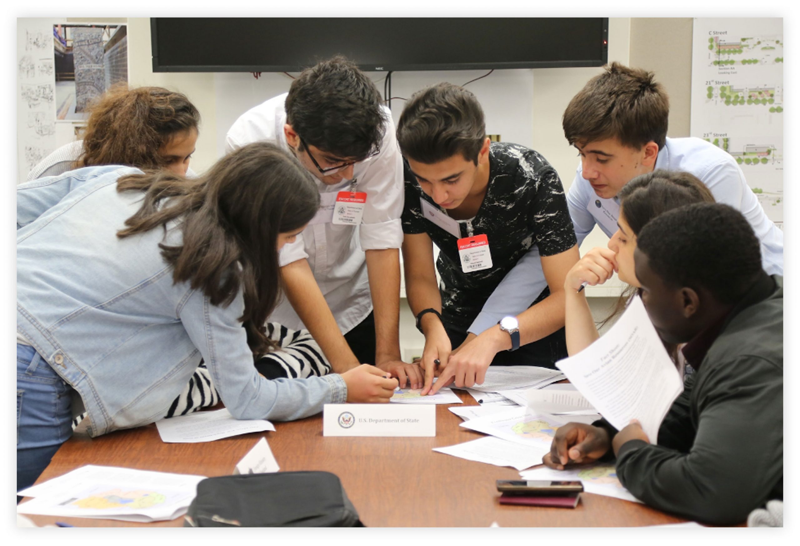 A group of students around a table looking at papers, pointing, and discussing.