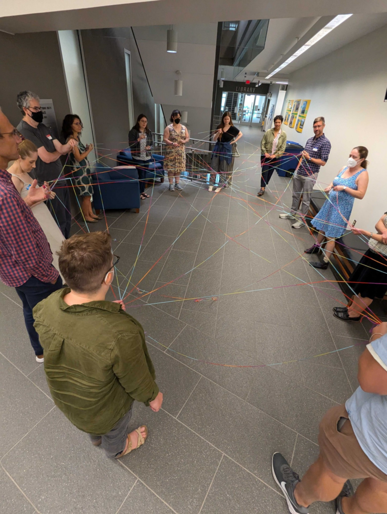 A group of people standing in a circle holding yarn to create a network graph